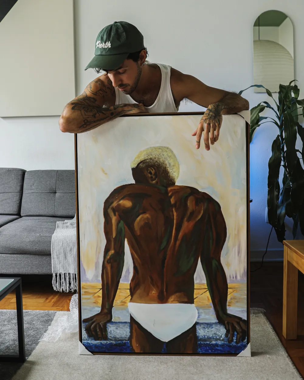 Guilherme holding up one of his paintings: a figure seen from behind, in warm browns.