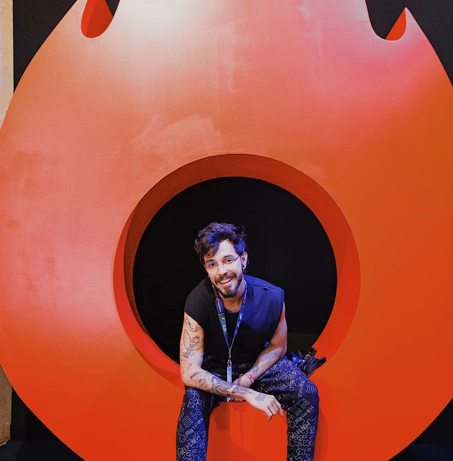 Guilherme seated inside the round opening of a large orange sculpture at the Hotmart office.
